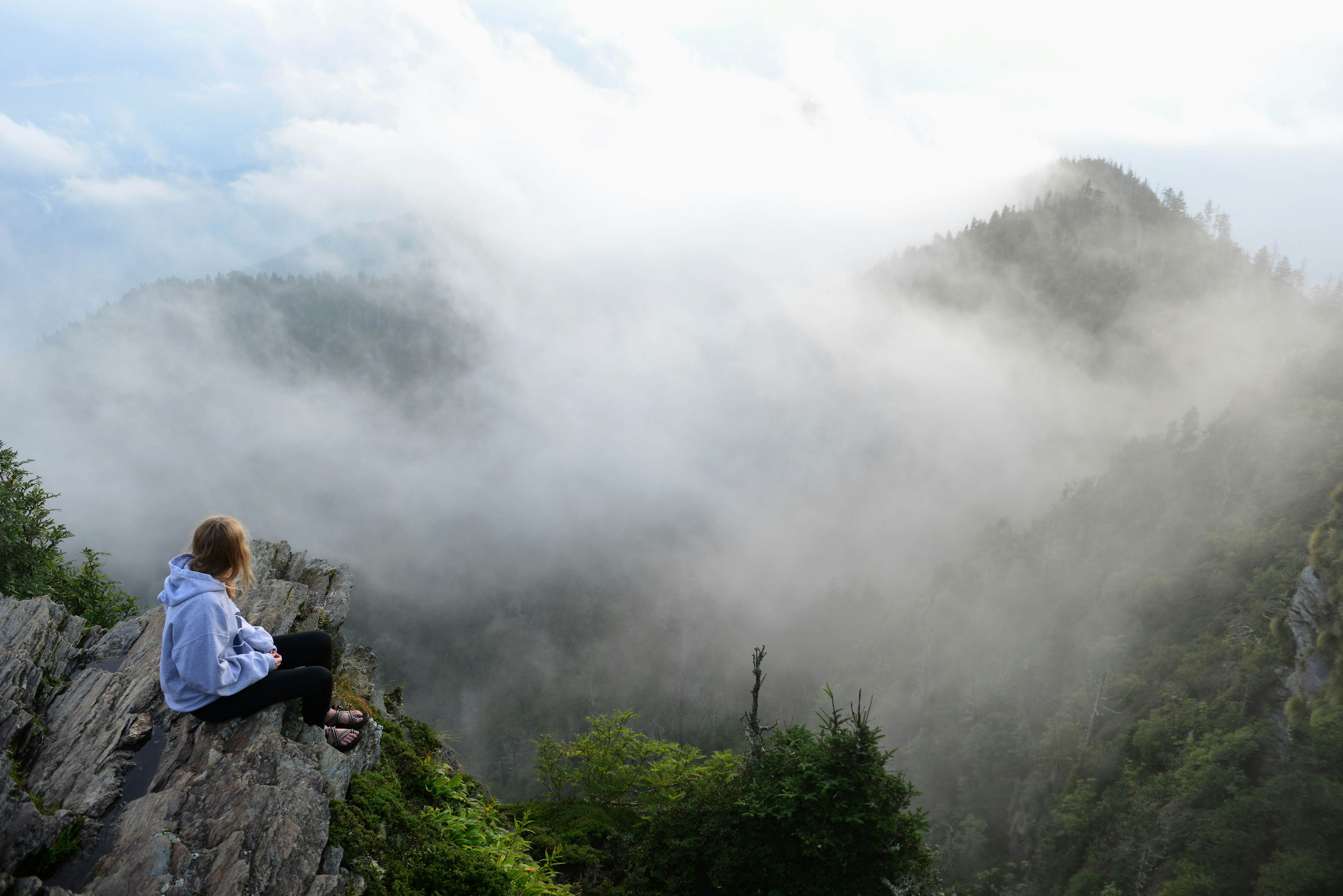 A teenage girl sits and watches drifting clouds at the summit of Mount LeConte in the Great Smoky Mountains National Park.